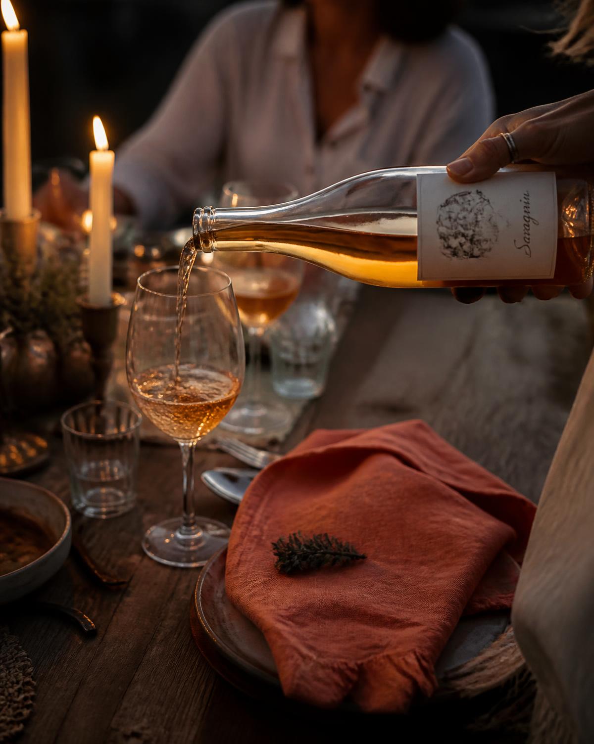 Hands pouring wine across a candlelit table