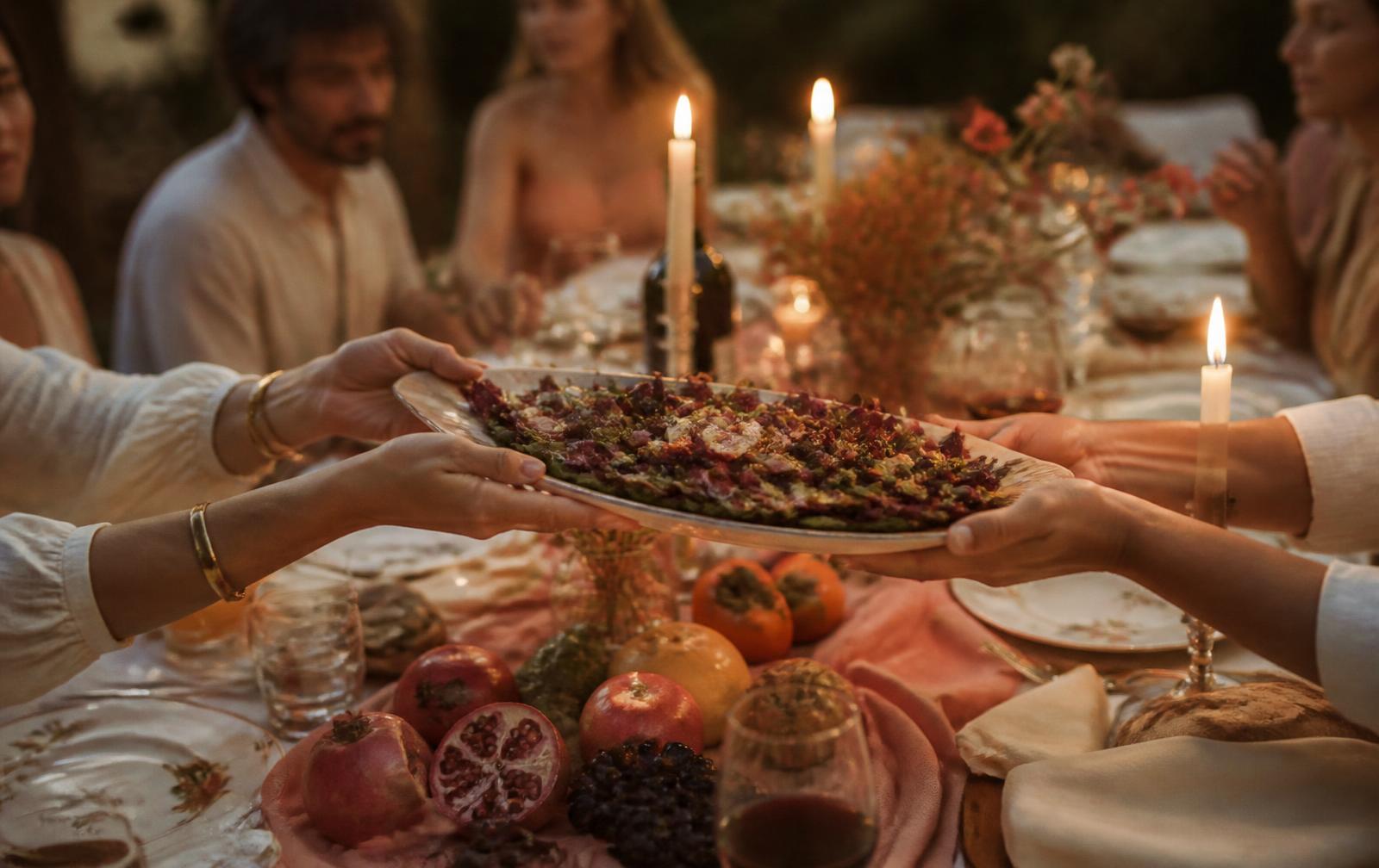 A platter of food passed between hands at a candlelit table